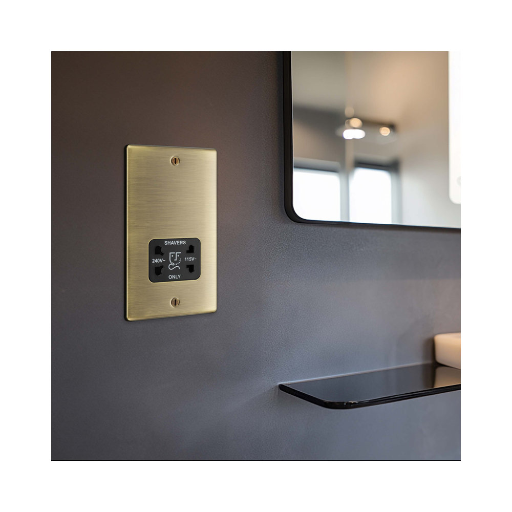 Brass shaver socket outlet on a gray wall with a mirror reflection.