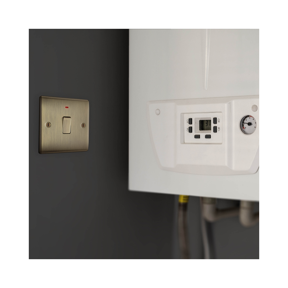 White boiler against a gray wall with a brass light switch and indicator.